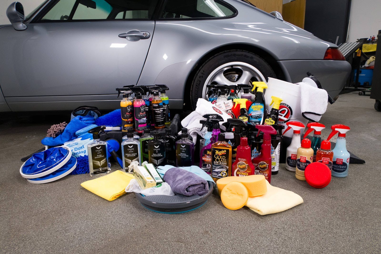 2. Assorted tools from a car detailing kit laid out on a garage floor, including foam cannon, microfiber mitt, and soap bottles.