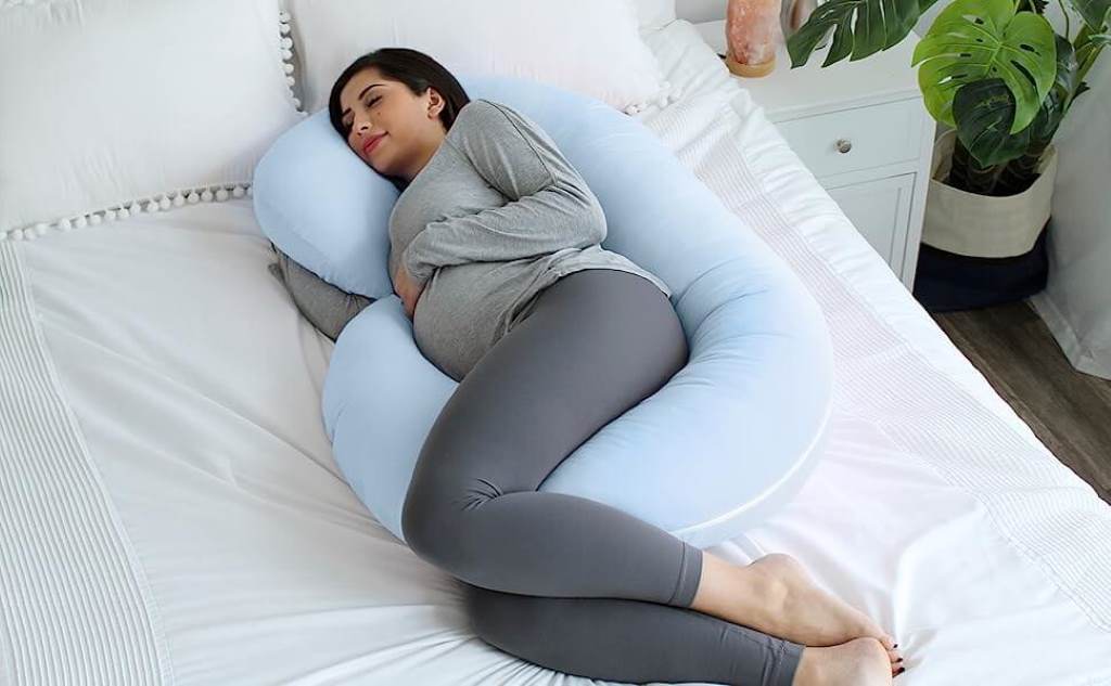 Side view of a mom-to-be lounging on a C-shaped maternity support pillow during afternoon rest.